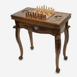 Puede incluir: Una mesa de juego de madera con tallas intrincadas y un tablero de ajedrez en la parte superior. La mesa tiene cuatro patas con cabezas de águila talladas en la base.