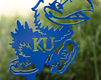 May include: Blue metal silhouette of a bird with the letters "KU" in the center. The bird is in a running pose with its wings spread out.