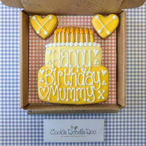 May include: A yellow and white decorated cookie in the shape of a birthday cake with the text "Happy Birthday Mummy" and two yellow heart-shaped cookies with an X design.
