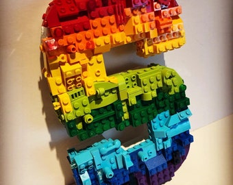 May include: A vibrant, rainbow-hued letter 'S' made from interlocking plastic bricks. The colours transition from red to orange, yellow, green, blue, and purple. The bricks are arranged to form the curved shape of the letter.