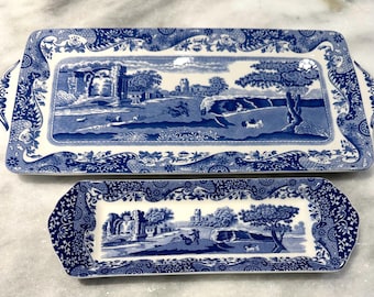 Puede incluir: Dos bandejas de servicio rectangulares de cerámica con un patrón de transferencia azul y blanco. El diseño representa un paisaje con ruinas, árboles y figuras. Ambas bandejas tienen asas ornamentadas y un borde floral decorativo.