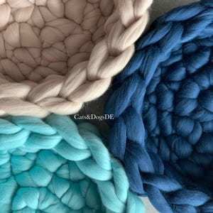 May include: Three round, chunky knit baskets in beige, dark blue, and turquoise. Each basket features a thick, braided rim and a woven base made from soft, oversized yarn. The text "Cats&DogsDE" is printed in white in the center of the image.