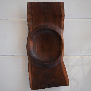 May include: A dark brown wooden bowl with a natural edge, carved from a single piece of wood. The bowl has a deep, round shape and is perfect for serving snacks or dips.