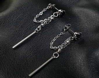 May include: A pair of silver earrings with a chain and a long, thin bar hanging from each. The earrings have a small black bead at the end of the chain and a small black flower at the top.