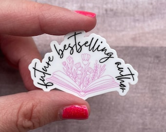 May include: White sticker with a pink open book with flowers inside. The text "future bestselling author" is written around the book.