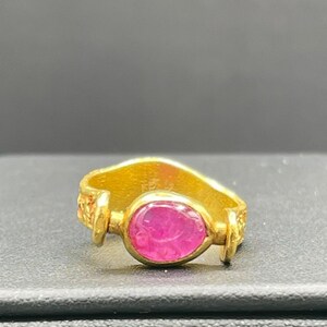 May include: A gold ring with a pink oval gemstone set in a textured band.