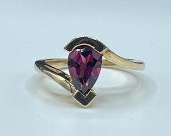 May include: A gold ring with a pear-shaped, dark red gemstone set in a twisted band.