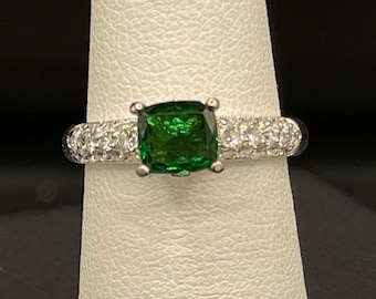 May include: A silver ring featuring a green gemstone surrounded by smaller white gemstones.