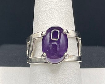 May include: A silver ring with an oval-shaped amethyst gemstone set in a delicate, openwork design.