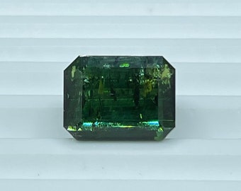 May include: A dark green emerald cut gemstone with a slight yellow hue.