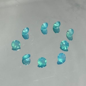 Puede incluir: Una colección de diez pequeñas piedras preciosas redondas de color turquesa dispuestas en círculo sobre una superficie blanca.