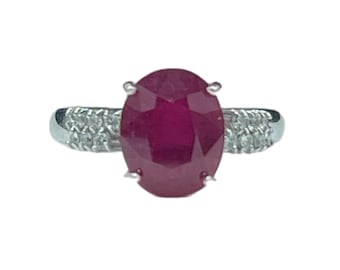 May include: A silver ring featuring a large oval ruby gemstone surrounded by smaller diamonds.