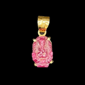 May include: A gold pendant featuring a pink, faceted gemstone. The gemstone is set in a gold frame and has a slightly irregular shape.
