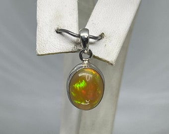 May include: A silver pendant featuring a round, iridescent opal gemstone with flashes of green, yellow, and orange.