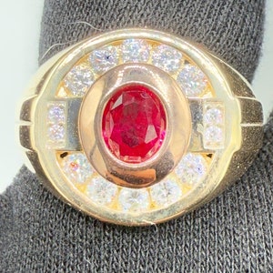 May include: A gold ring with a large red gemstone surrounded by smaller white gemstones.