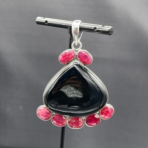 May include: A silver pendant featuring a black agate stone with a white crystal inside. The pendant is surrounded by six pink gemstones.