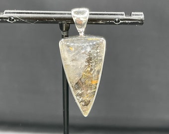 Puede incluir: Un colgante de plata con una piedra transparente de forma triangular con inclusiones marrones y doradas.