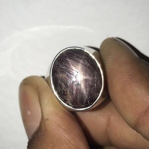 Può includere: Un anello d'argento con una pietra ovale di colore rosso scuro con un motivo a forma di stella.