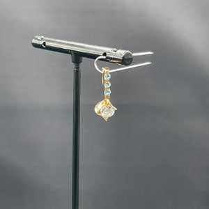 May include: A gold earring with a single clear stone and a row of smaller blue stones hanging from the bottom.