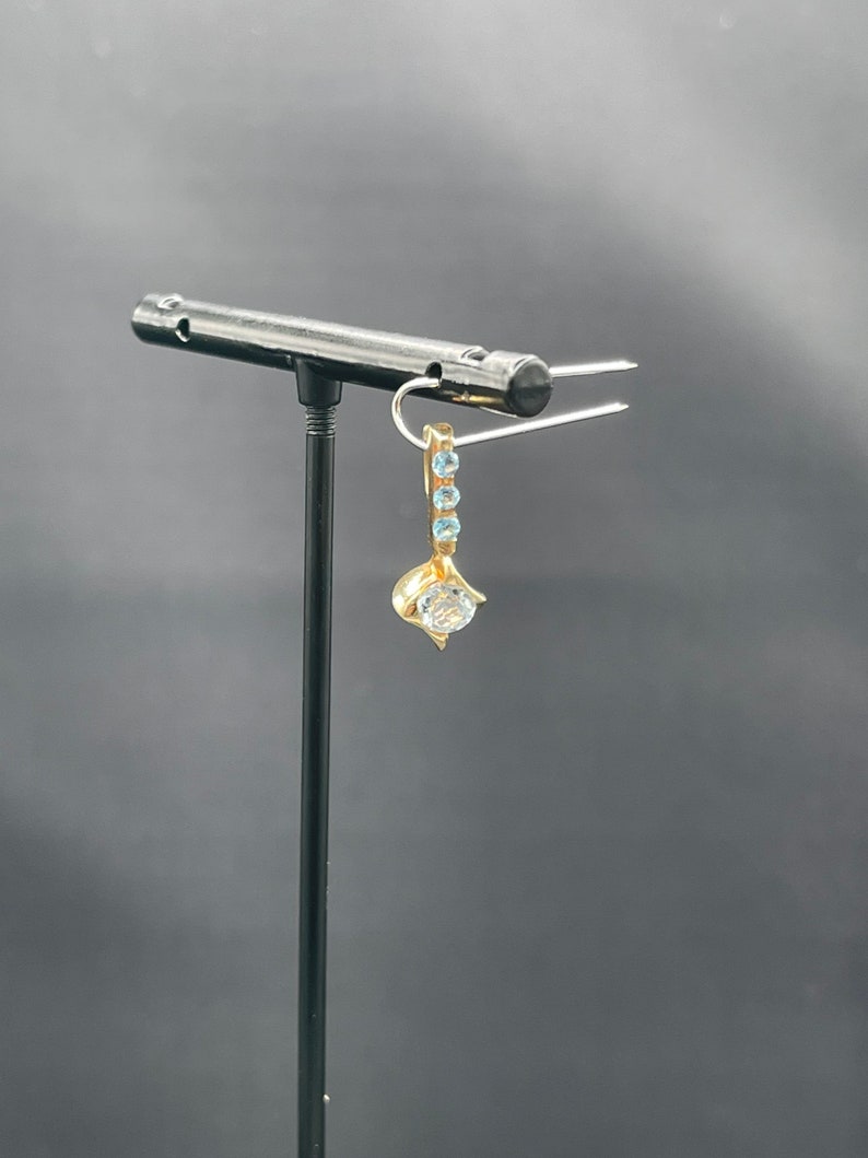 May include: A gold earring with a single clear stone and a row of smaller blue stones hanging from the bottom.