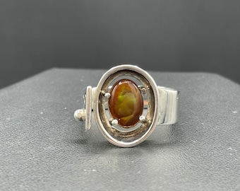 May include: A silver ring with a brown and green oval gemstone set in a geometric design.