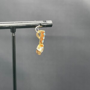 May include: Gold charm with blue stones, hanging from a black display stand.