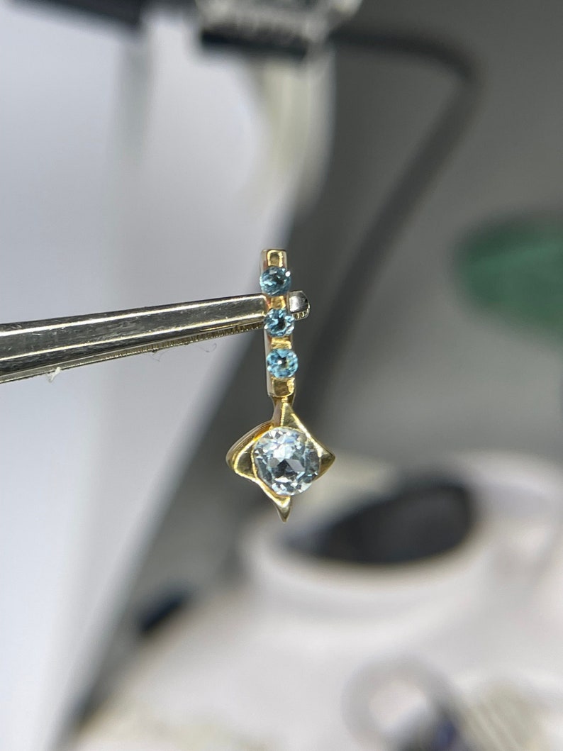 May include: A gold pendant featuring a blue gemstone and smaller blue gemstones on a gold chain.
