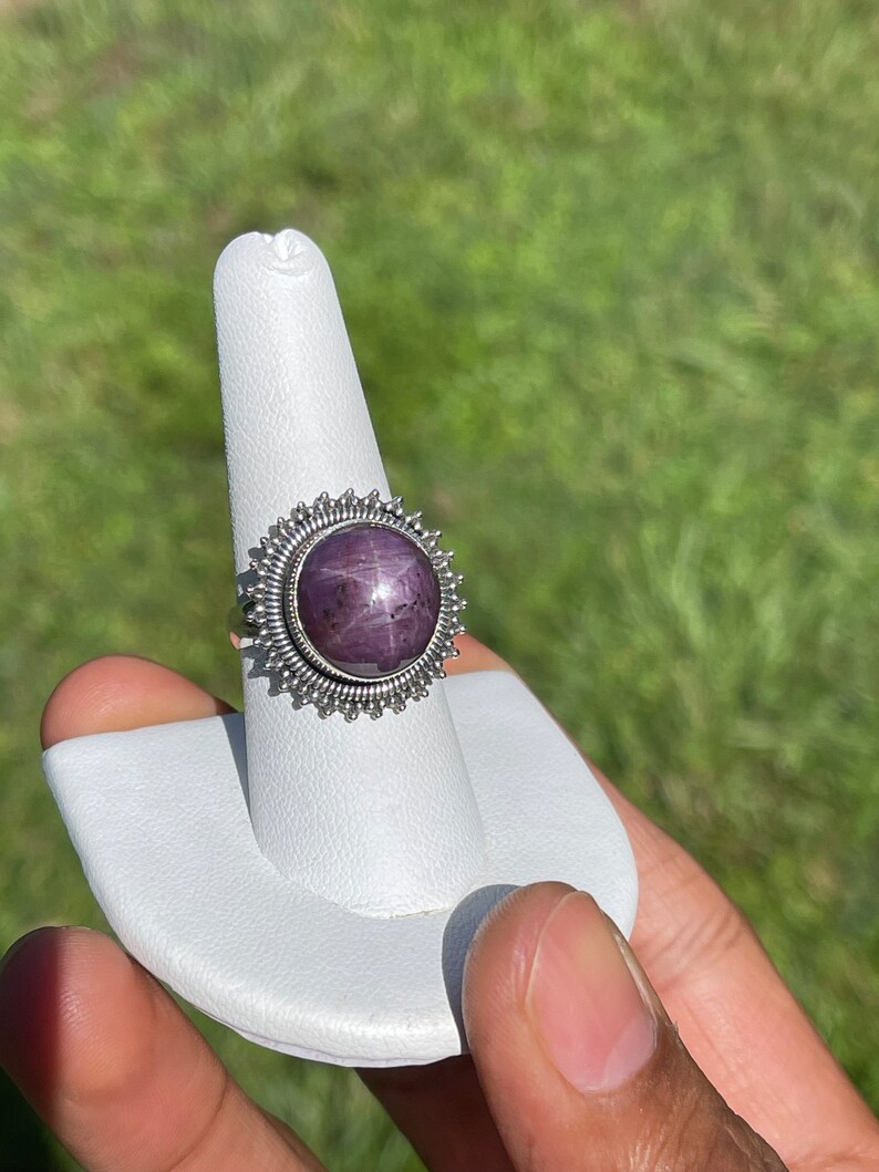 May include: A silver ring with a purple star ruby gemstone set in a silver sunburst design.