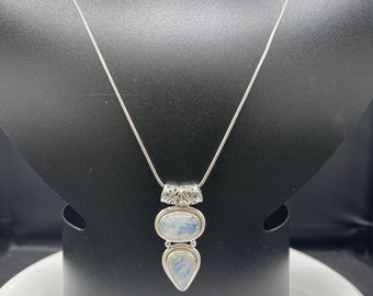 May include: A silver chain necklace with a pendant featuring two blue moonstone stones set in silver. The larger stone is oval-shaped, and the smaller stone is teardrop-shaped.