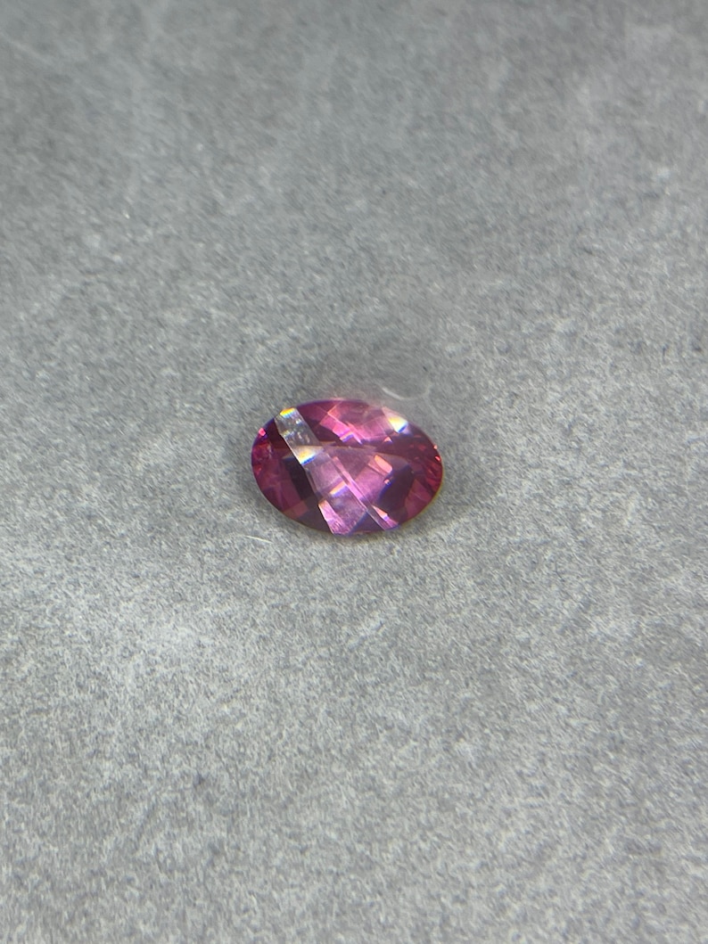 Puede incluir: Una piedra preciosa ovalada de color rosa con un ligero brillo.