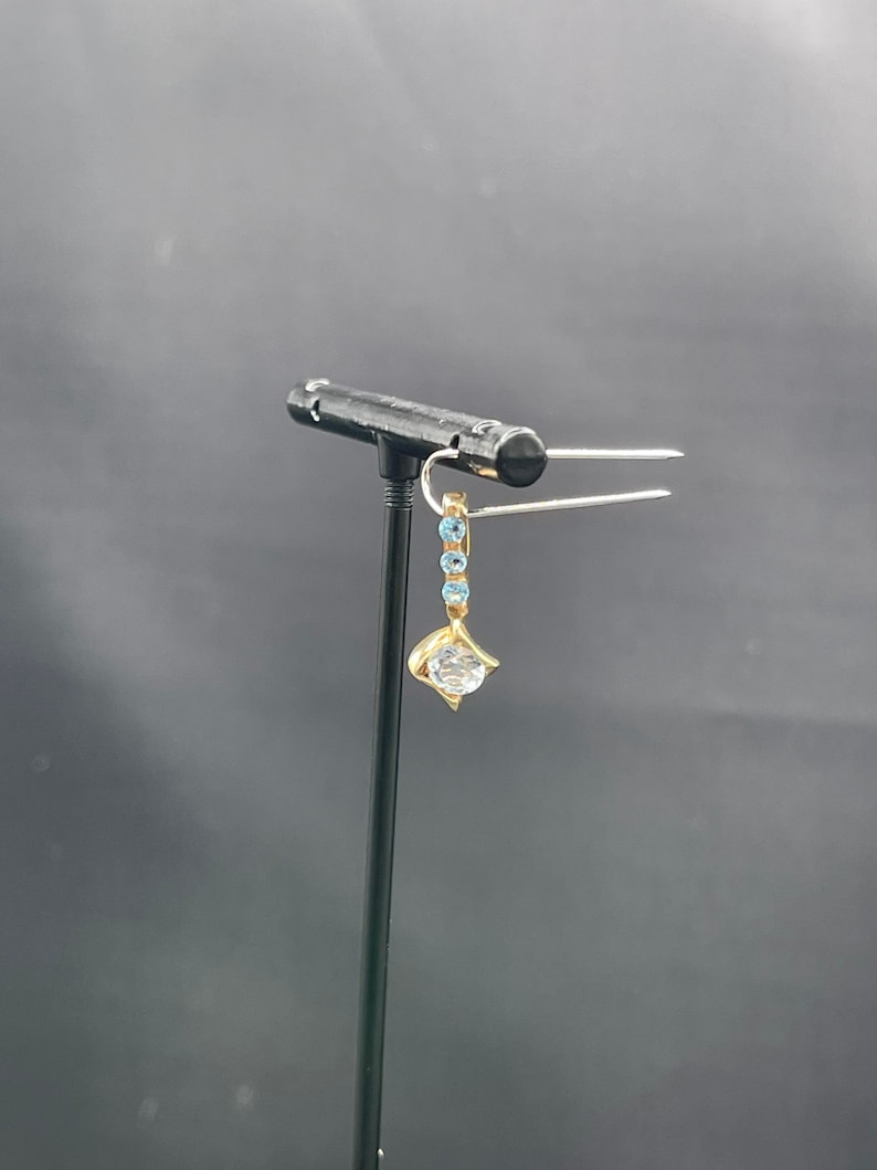 May include: A gold earring with a clear round gemstone and blue accents.