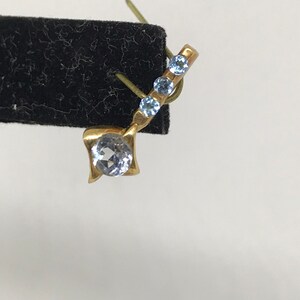 May include: A gold earring with a single round clear stone and three smaller blue stones.