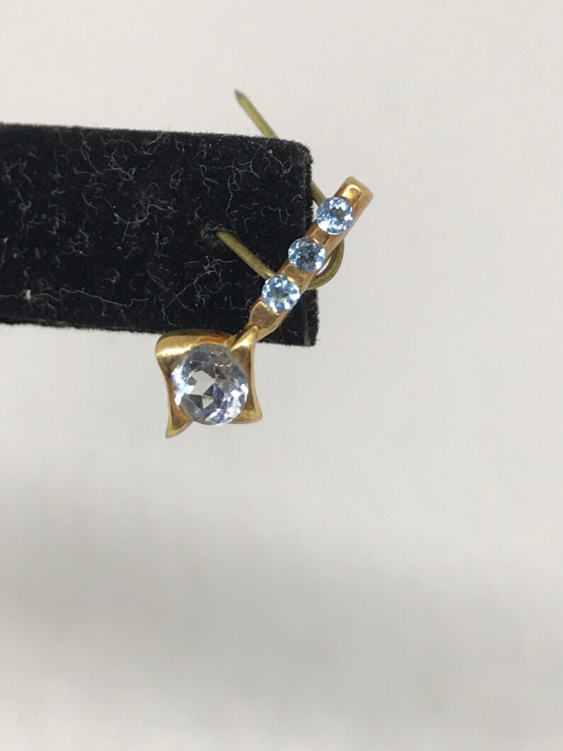 May include: A gold earring with a single round clear stone and three smaller blue stones.