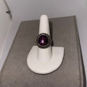 May include: A silver ring with a purple starburst gemstone set in a sunburst design.
