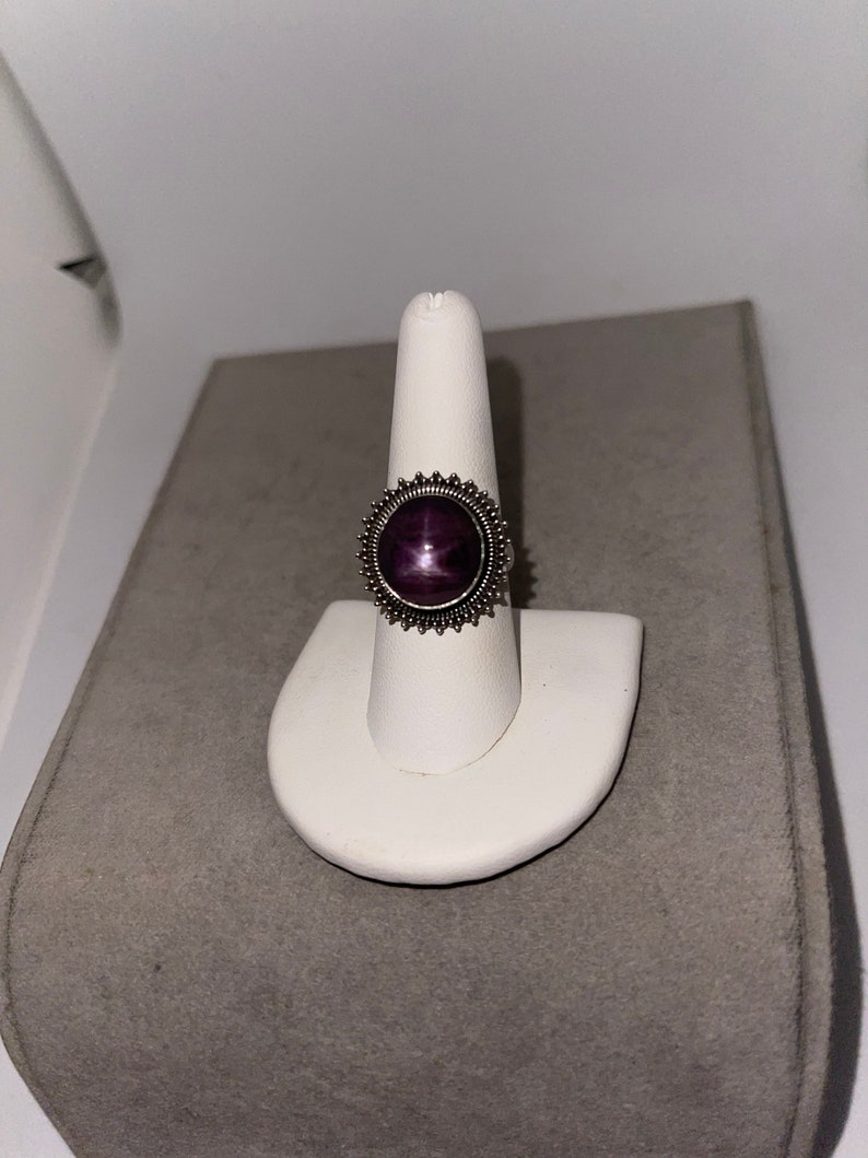 May include: A silver ring with a purple starburst gemstone set in a sunburst design.