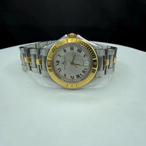 May include: A silver and gold-toned wristwatch with a silver dial and gold Roman numeral hour markers. The watch has a date window at the 3 o'clock position and a two-tone stainless steel and gold band. The watch is displayed on a white surface.