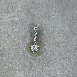 May include: A gold pendant featuring a single round blue gemstone and a row of smaller blue gemstones.