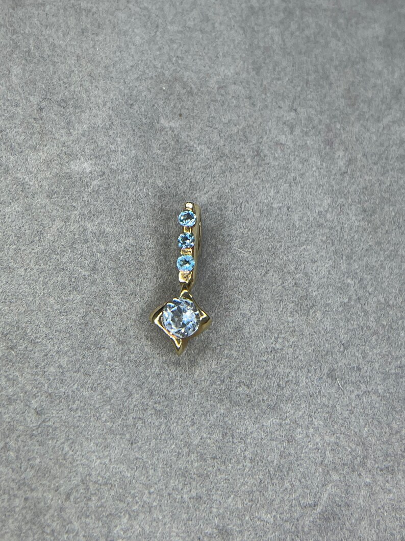 May include: A gold pendant featuring a single round blue gemstone and a row of smaller blue gemstones.