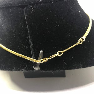 May include: A gold chain necklace with a lobster clasp closure. The chain is on a black velvet display stand.