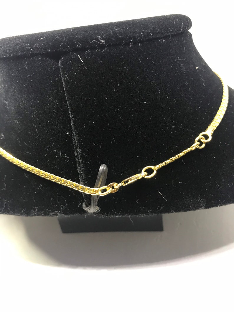 May include: A gold chain necklace with a lobster clasp closure. The chain is on a black velvet display stand.