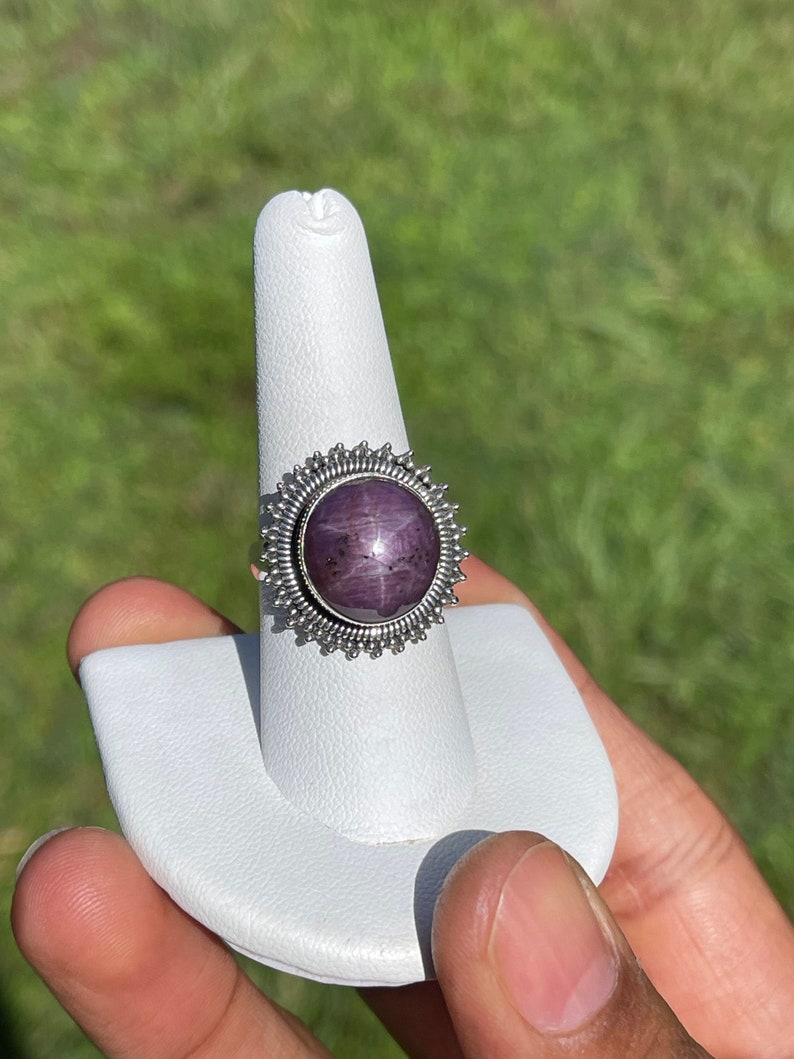 May include: A silver ring with a purple star ruby gemstone set in a starburst design.