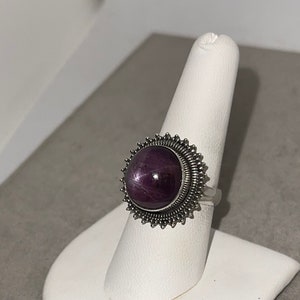 May include: A silver ring with a large, round, purple gemstone set in a starburst design.