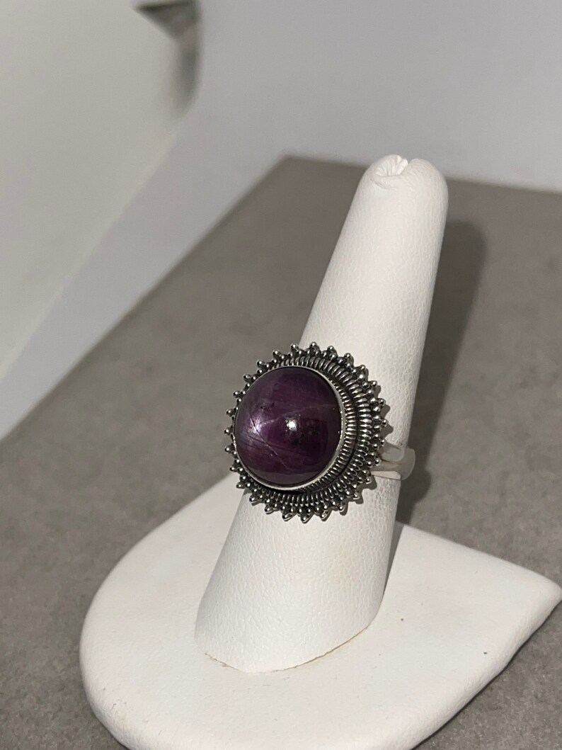 May include: A silver ring with a large, round, purple gemstone set in a starburst design.