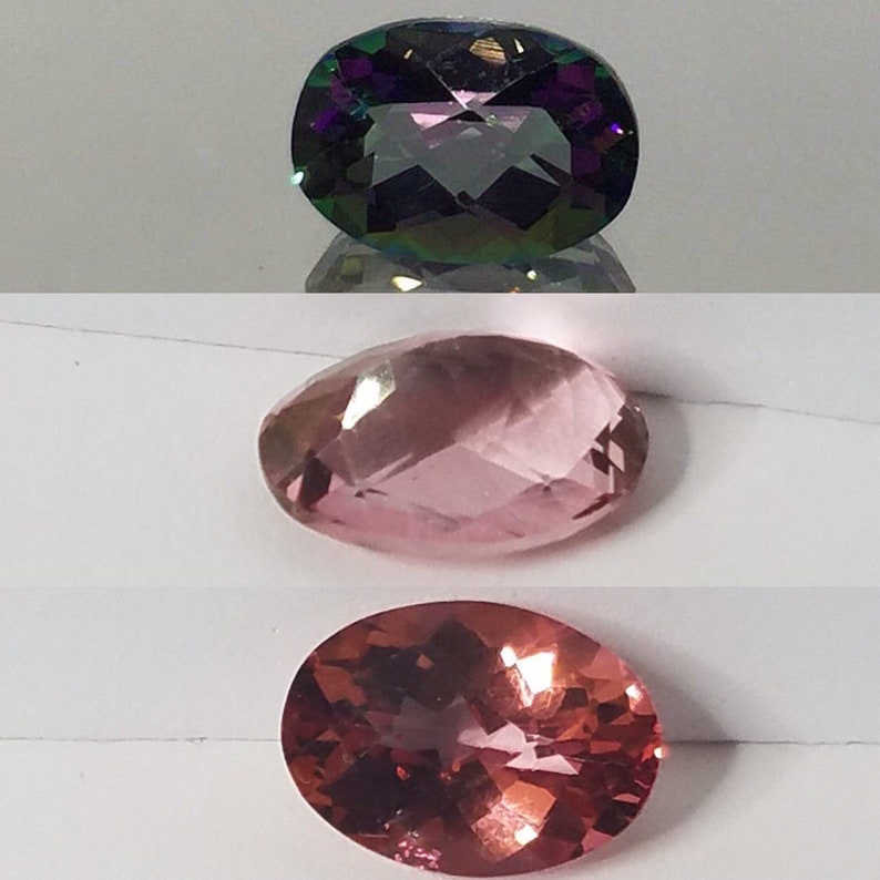 Puede incluir: Tres piedras preciosas de forma ovalada. La piedra superior es de color morado oscuro con matices iridiscentes verdes y azules. La piedra del medio es de color rosa claro con un ligero brillo. La piedra inferior es de color rosa oscuro con un ligero brillo.