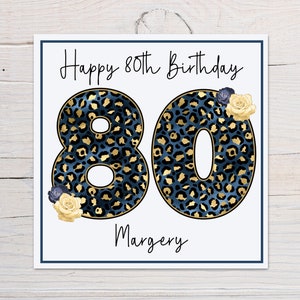 Puede incluir: Una tarjeta blanca con el texto "Happy 80th Birthday" y el n&uacute;mero 80 en estampado de leopardo azul y dorado. El nombre "Margery" est&aacute; escrito debajo del n&uacute;mero 80.