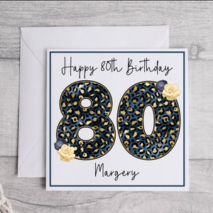 Puede incluir: Una tarjeta blanca con un dise&ntilde;o de estampado de leopardo azul y dorado. La tarjeta dice "Happy 80th Birthday" y "Margery".