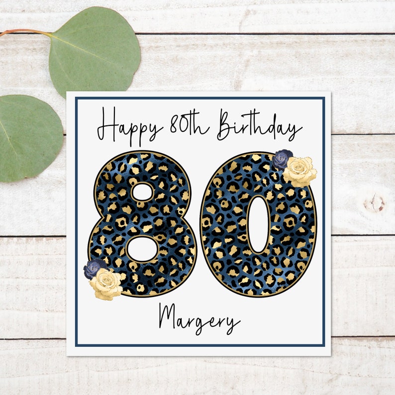 Puede incluir: Una tarjeta blanca con un borde azul y el texto "Happy 80th Birthday" en letra cursiva negra. El n&uacute;mero 80 est&aacute; en letras grandes, negritas, de estampado de leopardo azul y dorado. El nombre "Margery" est&aacute; escrito en letra cursiva negra debajo del n&uacute;mero 80.