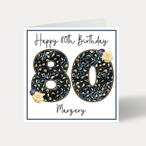 Puede incluir: Una tarjeta blanca con un borde azul y el texto "Happy 80th Birthday" en letra cursiva negra. El n&uacute;mero 80 est&aacute; en letras grandes, negritas, de estampado de leopardo azul y dorado. El nombre "Margery" est&aacute; escrito en letra cursiva negra debajo del n&uacute;mero 80. Hay peque&ntilde;as flores amarillas y azules en la tarjeta.