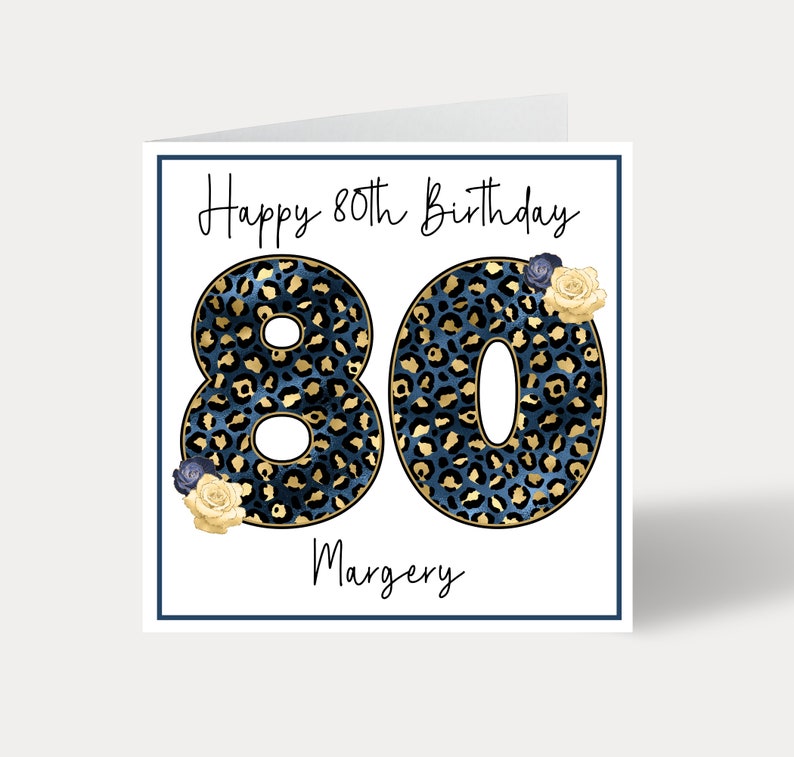 Puede incluir: Una tarjeta blanca con un borde azul y el texto "Happy 80th Birthday" en letra cursiva negra. El n&uacute;mero 80 est&aacute; en letras grandes, negritas, de estampado de leopardo azul y dorado. El nombre "Margery" est&aacute; escrito en letra cursiva negra debajo del n&uacute;mero 80. Hay peque&ntilde;as flores amarillas y azules en la tarjeta.