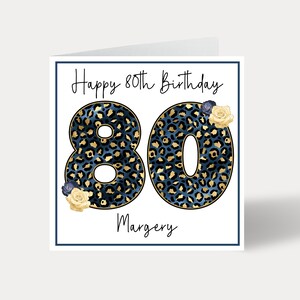 Puede incluir: Una tarjeta blanca con un borde azul y el texto "Happy 80th Birthday" en letra cursiva negra. El n&uacute;mero 80 est&aacute; en letras grandes, negritas, de estampado de leopardo azul y dorado. El nombre "Margery" est&aacute; escrito en letra cursiva negra debajo del n&uacute;mero 80. Hay peque&ntilde;as flores amarillas y azules en la tarjeta.